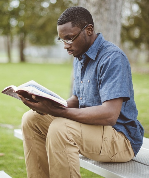 Young African-American male sitting on the bench and reading the Bible